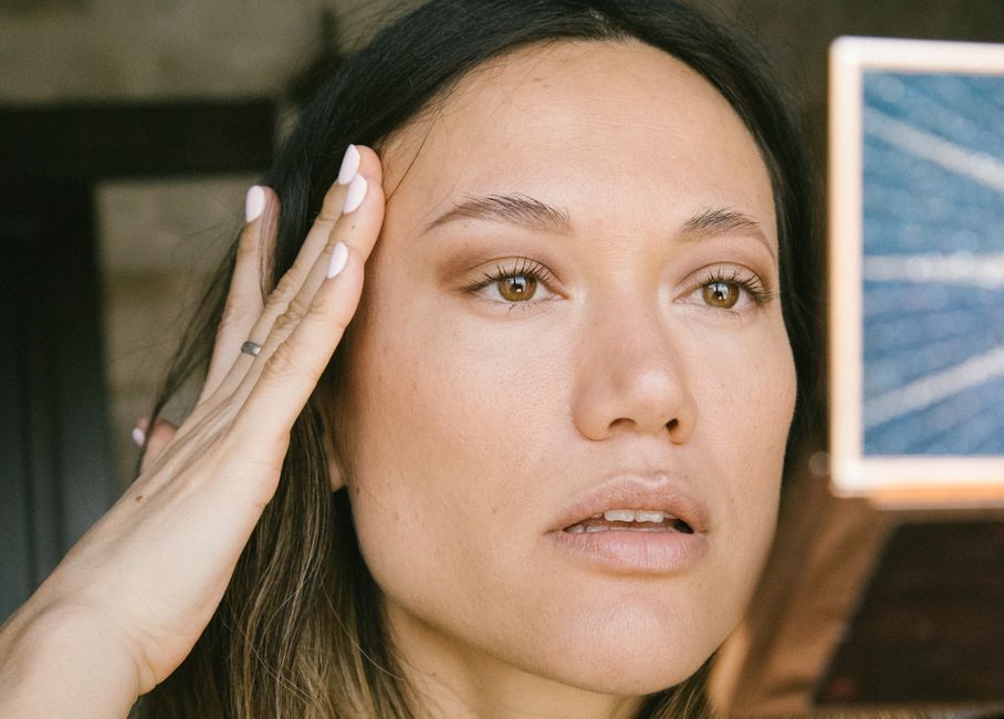 A natural close-up portrait of a woman applying makeup in an indoor setting.