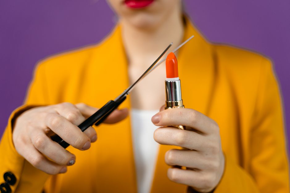 Close-up of a woman holding lipstick being cut with scissors, showing bold color contrast.