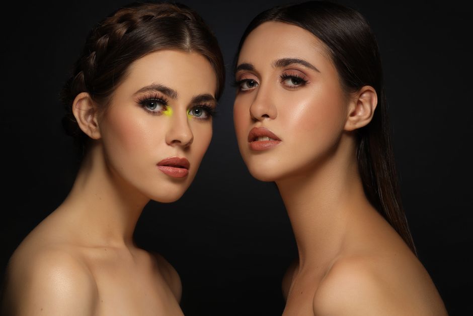 Close-up portrait of two women with flawless makeup and dark background.