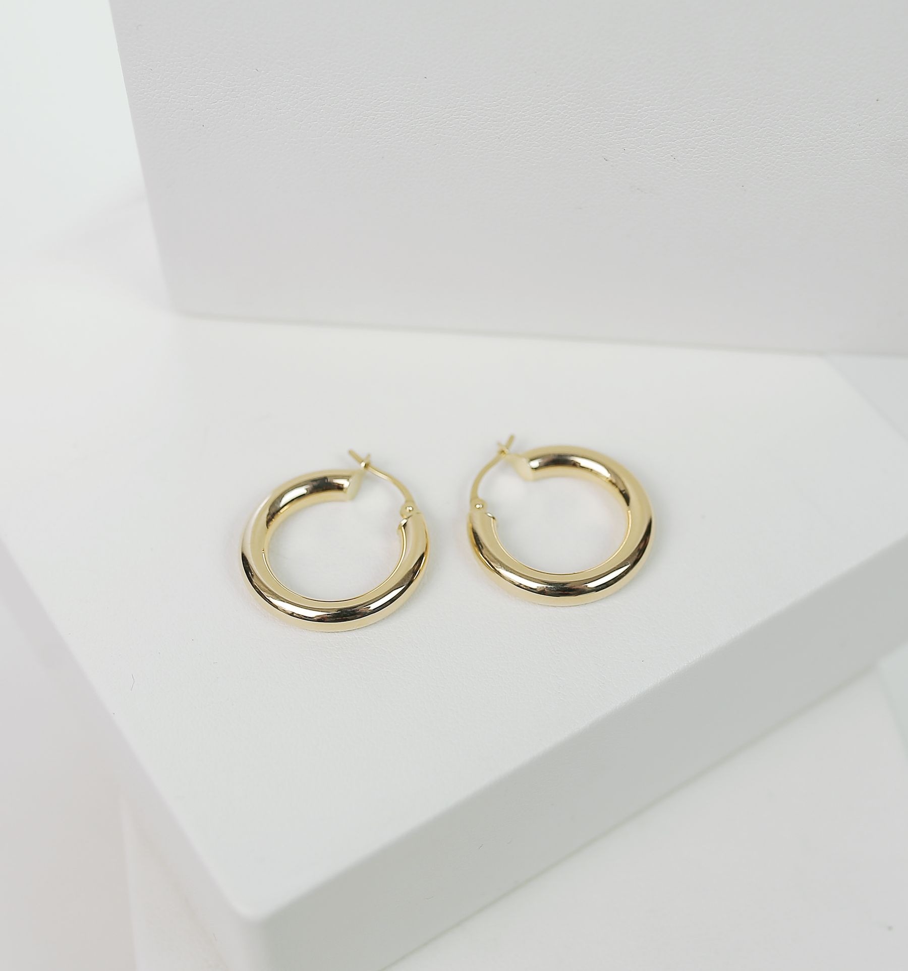 A pair of polished gold-colored hoop earrings resting on a stepped white display.