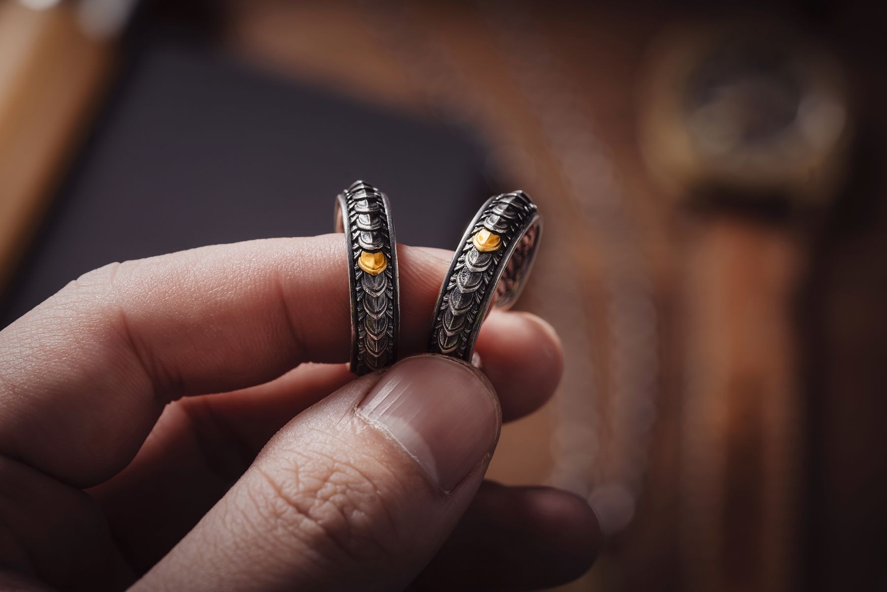 Hand holding two engraved silver-colored rings with small gold-colored accents; a two-tone jewelry connector example, with no metal-composition guarantee.