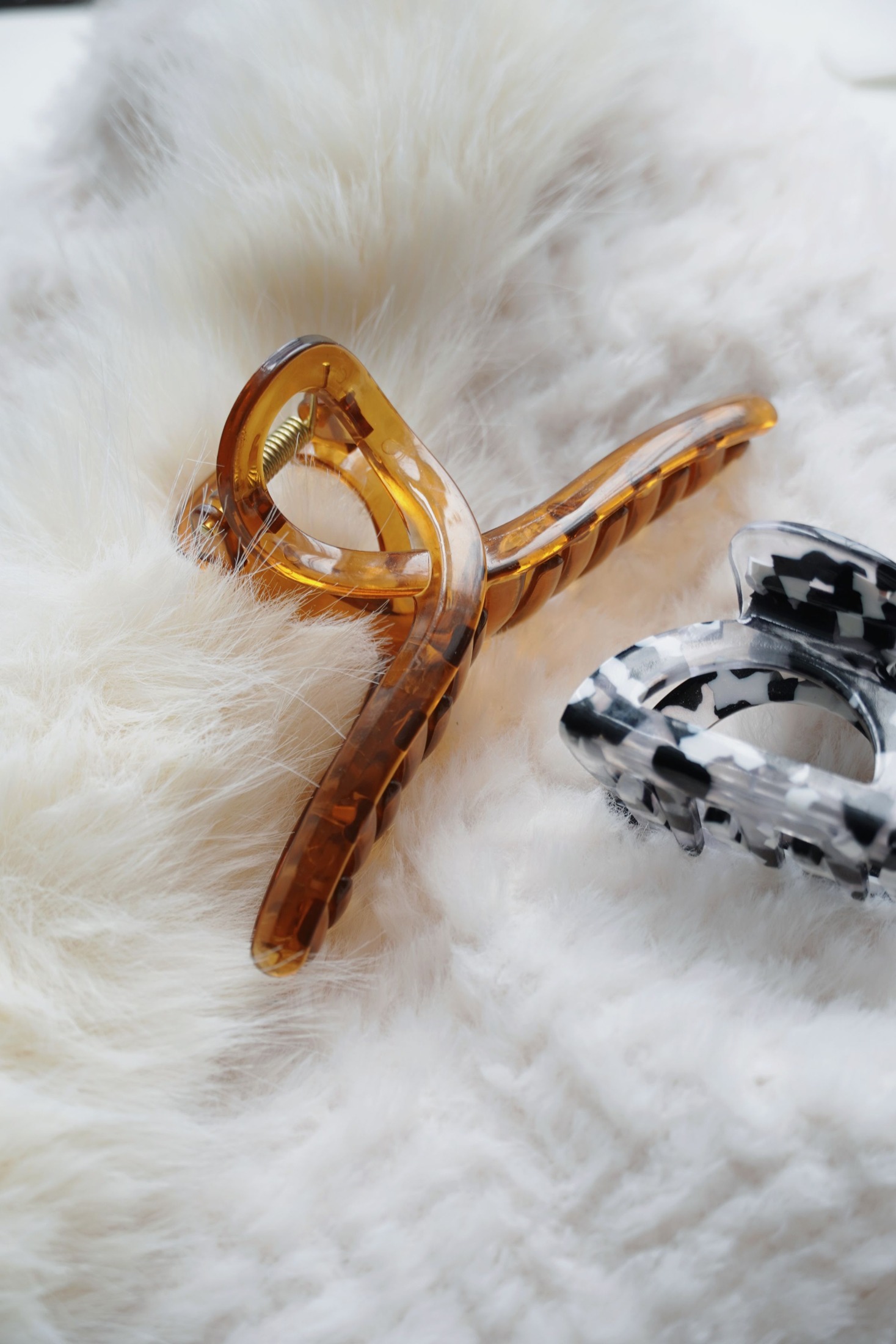 Amber translucent and black-and-white patterned claw hair clips resting on plush white fabric.