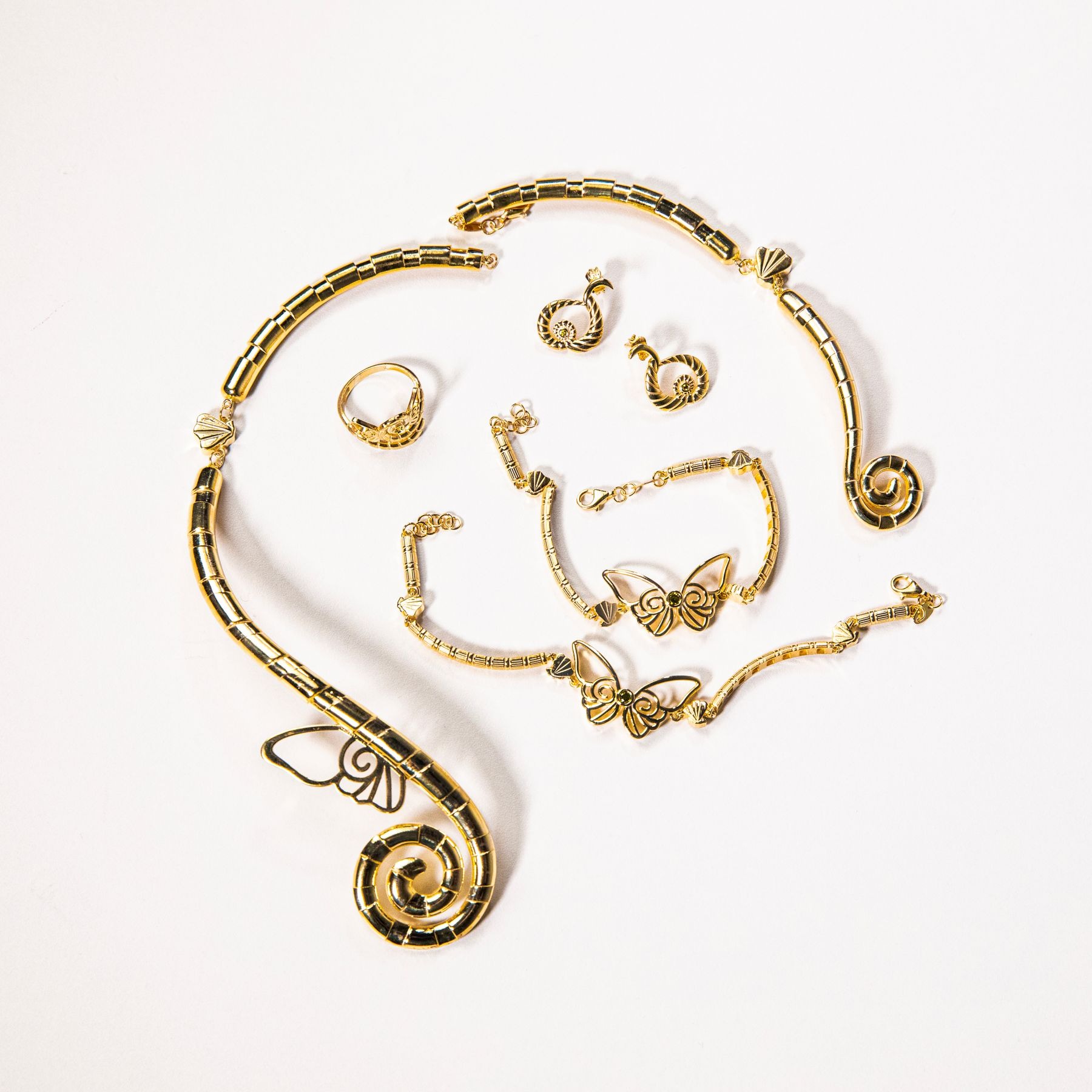 Gold-colored necklace, butterfly bracelets, spiral earrings and a ring arranged on white.