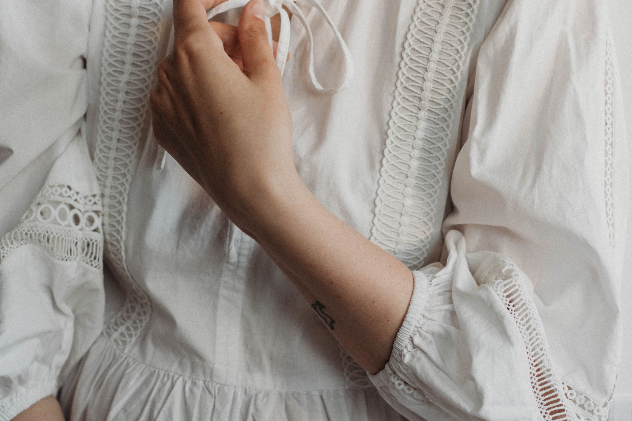 Close-up of a white embroidered summer dress with openwork trim, gathered cloth and a long cuffed sleeve; fabric and construction detail for checking coverage, without asserting that a lining is present.