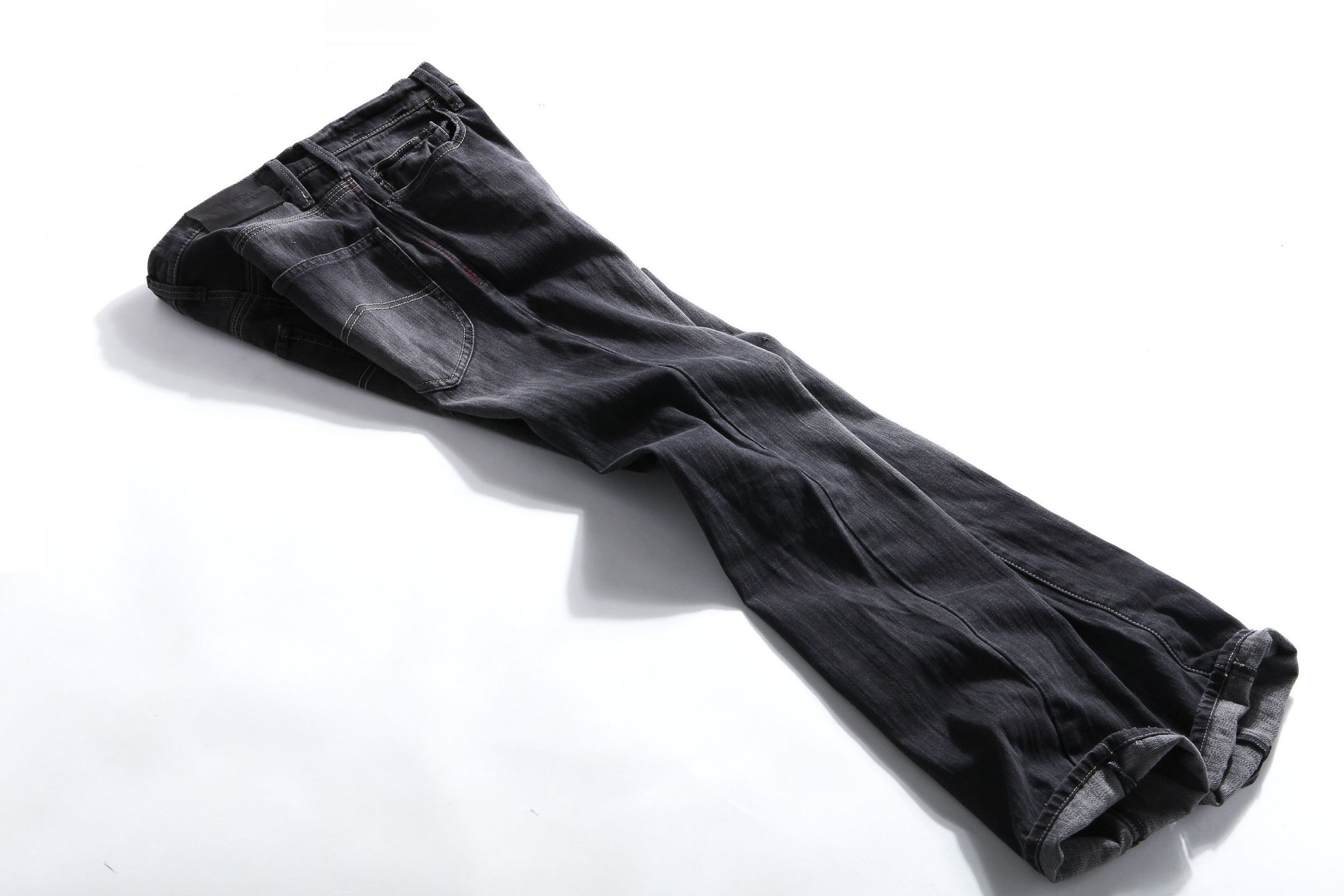 Folded charcoal-black jeans on white showing pockets, seams, belt loops and turned hems; a denim inspection component rather than a complete office outfit.