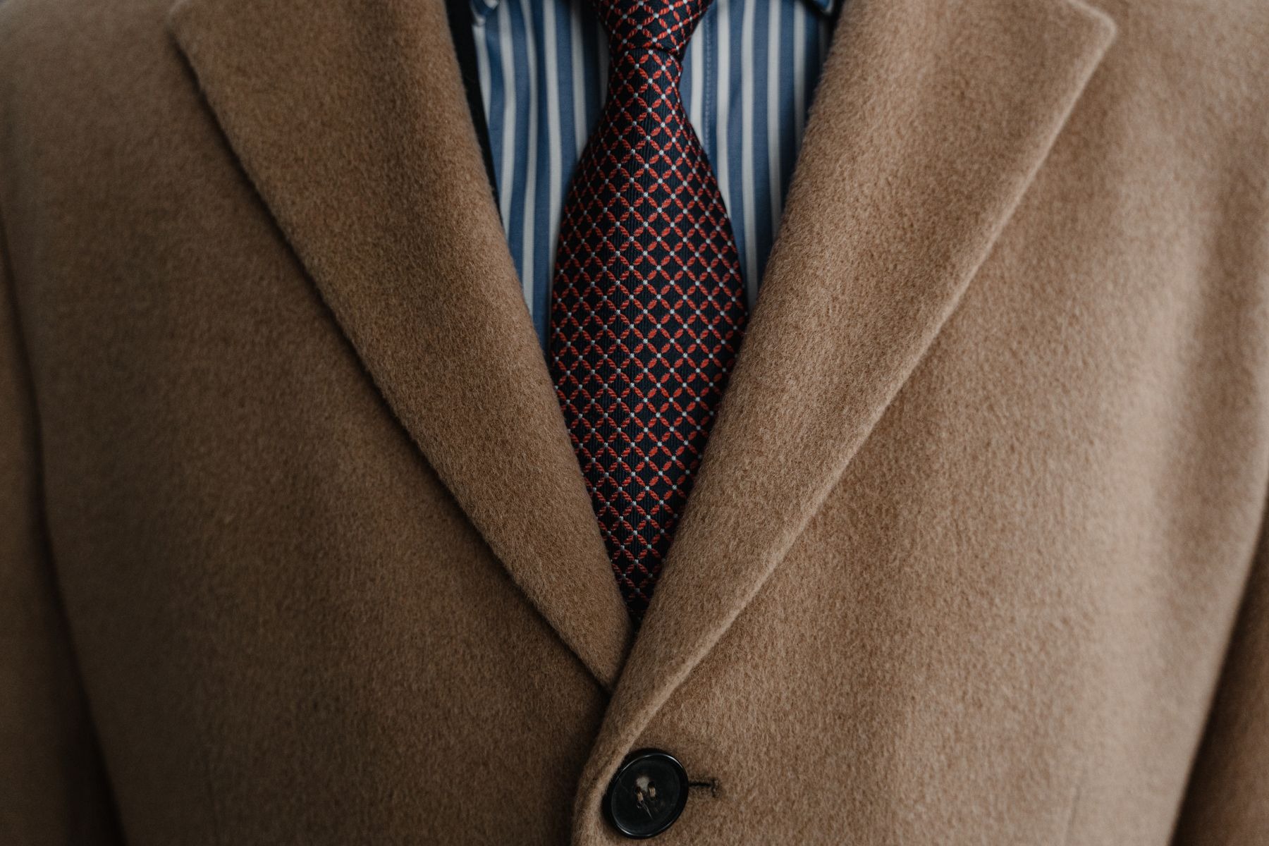 Close-up of a brown textured overcoat's lapels and front button over a striped shirt and patterned tie; primary source identifies a wool coat. Construction illustration only, not a readable care-label example.