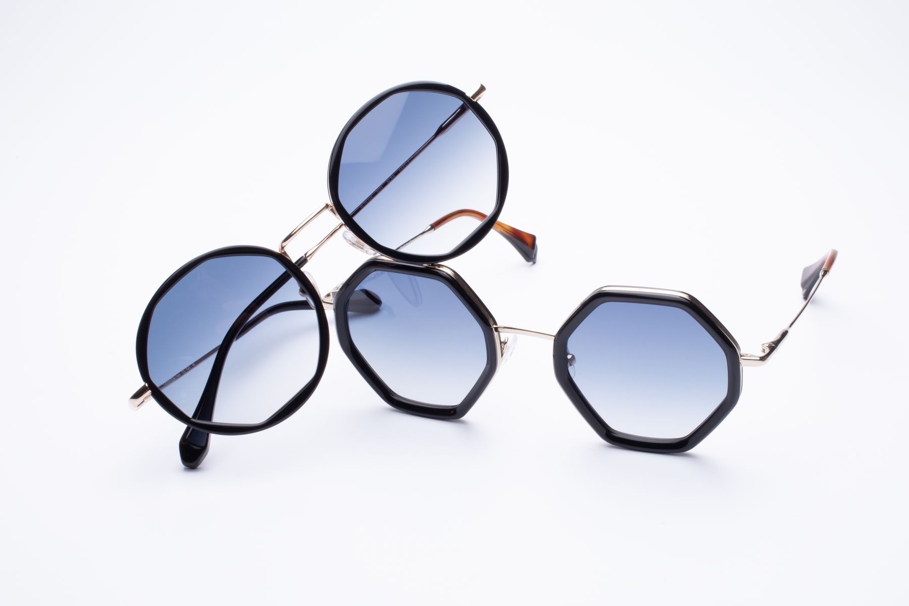 Two pairs of blue-tinted sunglasses on white, one with round frames and one with angular polygonal frames.
