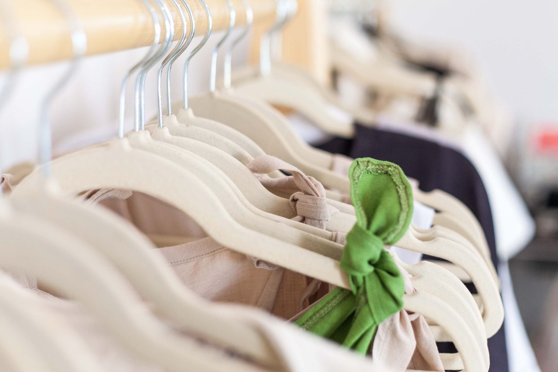 Close-up of cream plastic hangers supporting light-colored garments, including a bright green tied garment detail; distinct from the full rail feature.