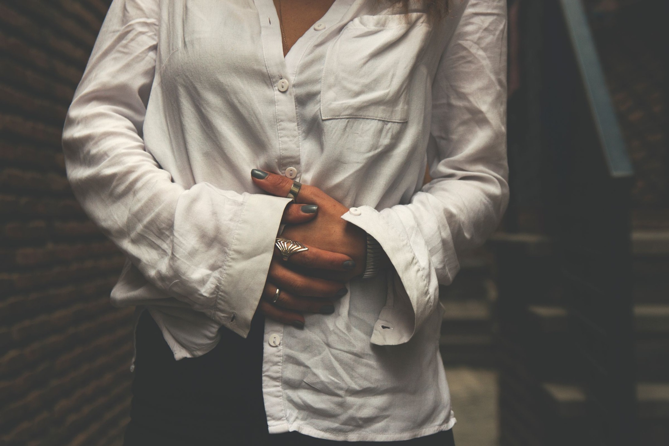 Torso close-up of an untucked white button-down with a chest pocket, extended cuffs and visible front hem; component illustration for inspecting shirt length and cloth before tucking.